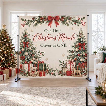 Our Little Christmas Miracle first birthday backdrop with evergreen branches, a red bow and gifts.