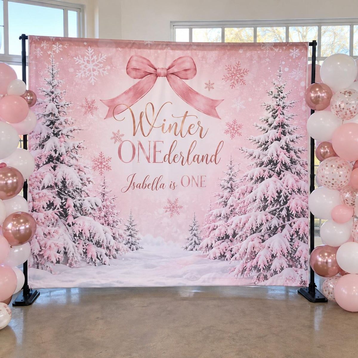 Pink Winter ONEderland first birthday backdrop with snowy trees, a bow and pink balloons.