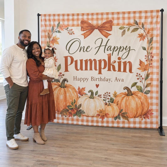 One Happy Pumpkin birthday backdrop with orange gingham, a bow and pumpkins, shown with a family for scale.