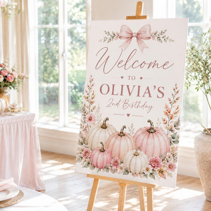 Pumpkin birthday welcome sign with Olivia's name, a pink bow, blush pumpkins and flowers, displayed on an easel.