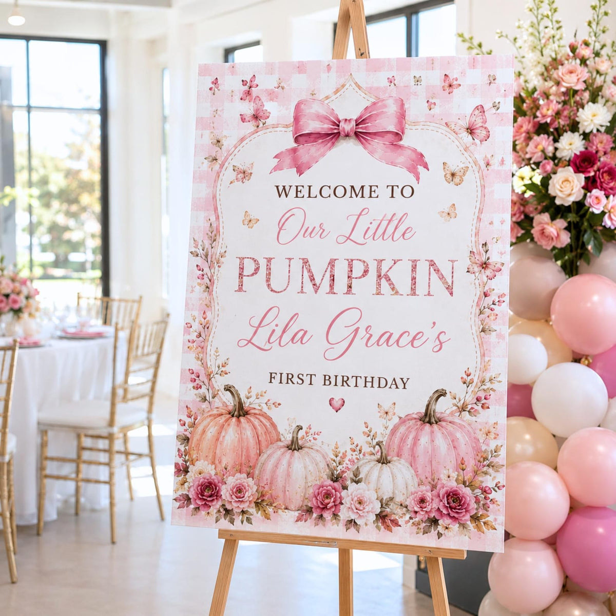 Pink floral Our Little Pumpkin first birthday sign displayed beside pink balloons.