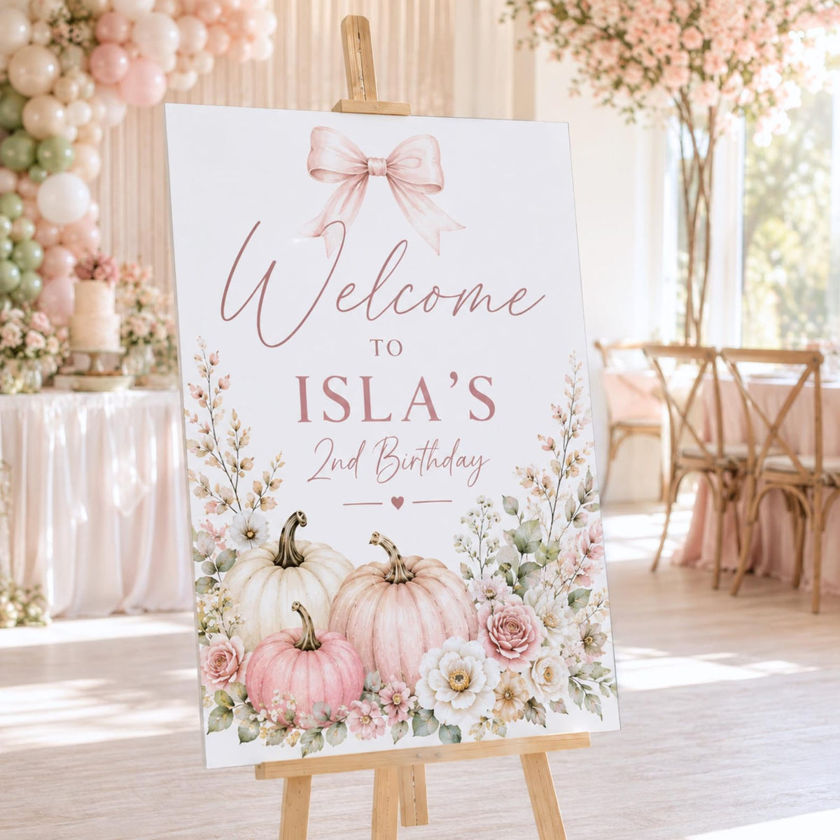 Isla's second birthday welcome sign with a pink bow, pastel pumpkins and flowers.